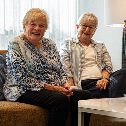 Two senior friends sitting on a brown couch in the lobby of Don Mills Retirement Residence